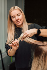 A hairdresser cuts a blonde's hair in a beauty salon. Women's haircut