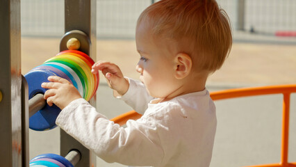 Portrait of little boy spinning colorful circles on abacus at playground. Children developments, kids education, baby learning.
