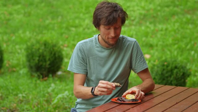 A bearded man is portrayed in a picturesque park, relishing a mouthwatering traditional Turkish dish of mussels with rice. The camera captures the delectable meal, showcasing the flavors and textures