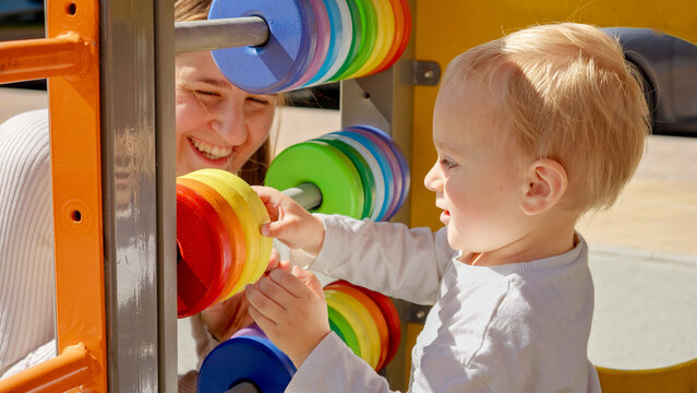 Young mother teaching her baby son using colorful abacus on playground. Children developments, kids education, baby learning.