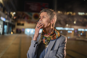 One caucasian senior woman stand in the city at night have a cigarette