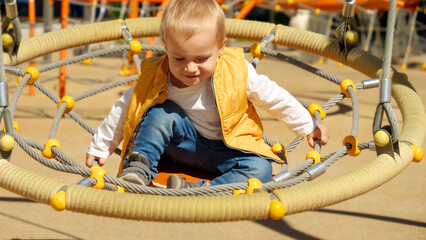 cute baby boy boy sitting in round swing and having fun on the playground. Children playing outdoor, kids outside, summer holiday and vacation.