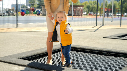 Happy mother with little son jumping and playing on trampoline at backyard. Happy parenting, family...