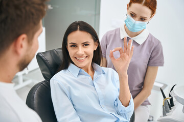 Smiling woman showing ok gesture sign sitting in orthodontic chair