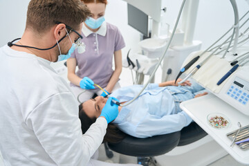 High-qualified stomatologist working on client tooth treatment or prosthesis - obrazy, fototapety, plakaty