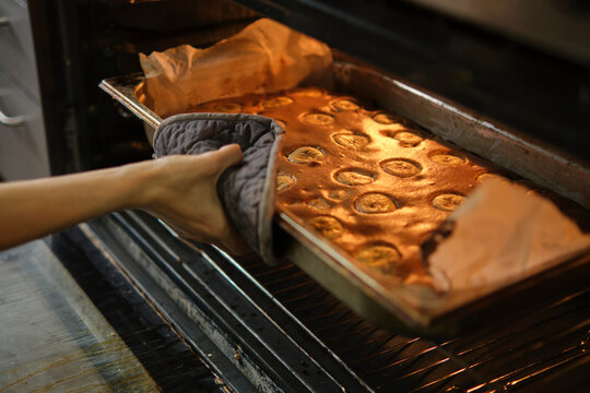 Cooking Banana Pie In The Oven. A Hand Holds A Hot Baking Sheet With A Tongs