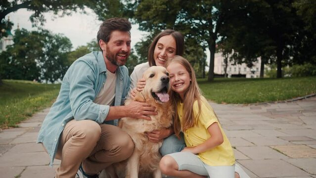 Smiling family of parents and little daughter hug golden dog