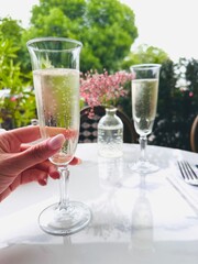 A glass of champagne in the hand of a Caucasian girl at a table in a cafe on the outside. 