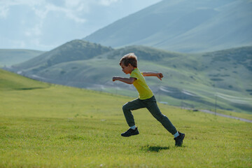 Boy running fast on a green meadow in the mountains