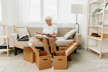 elderly woman sits on a sofa at home with boxes. collecting things with memories albums with photos...