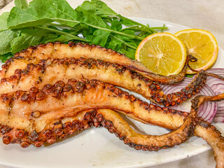 Octopuses, which have just come out of the Aegean Sea, are cooked on the grill fire and served on the plate with arugula, oregano, lemon and onions. Gokceada, Imbros island, Canakkale, Turkey
