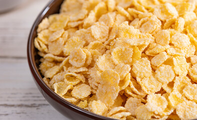 Ceramic bowl of corn flakes on white wood background with copy space. Traditional breakfast cereal. 