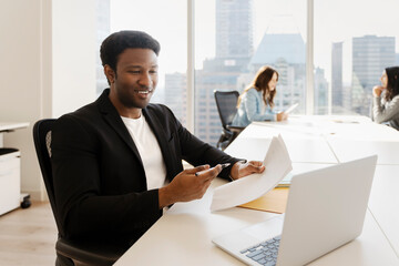 African businessman working, having video call using laptop, sitting at workplace in modern office