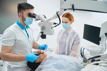 Young dentist in the clinic fills a tooth for client