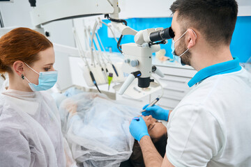 Naklejka na ściany i meble Doctor dentist treats a young female tooth under a microscope