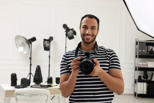 Young professional photographer with camera in modern photo studio, space for text