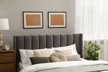 Comfortable bed with cushions, houseplant and frames in room. Stylish interior