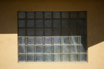 A basic yellow stucco wall is punctuated by a window made from a grid of glass blocks.