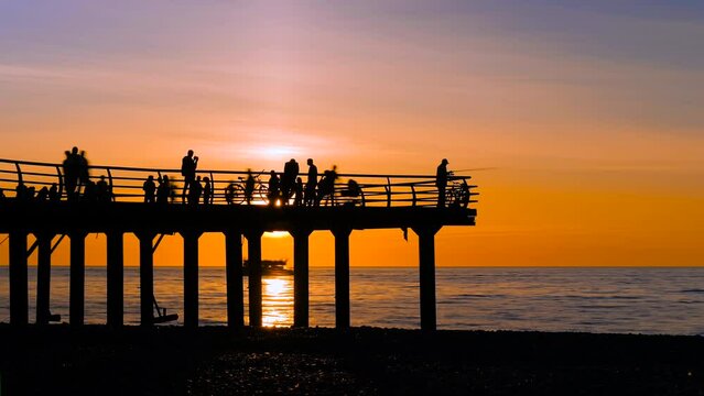 Timelapse: unrecognizable silhouettes of people are walking on the pier against the dramatic sky over the Black Sea at sunset. Vacation, peaceful, calm, summer, tropical and time lapse concept