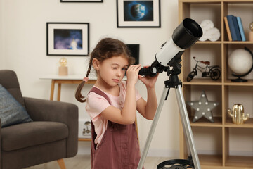 Cute little girl looking at stars through telescope in room