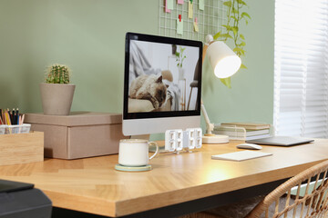 Stylish workplace with computer, laptop and lamp near olive wall at home