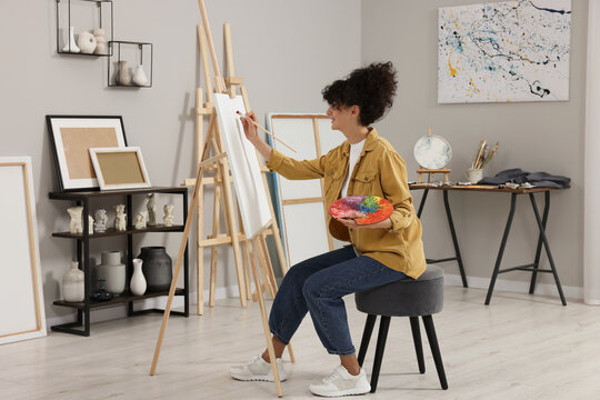 Young woman painting on easel with canvas in studio