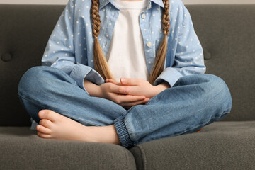 Little girl meditating on soft sofa indoors, closeup