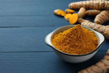 Bowl with turmeric powder and raw roots on blue wooden table, closeup. Space for text