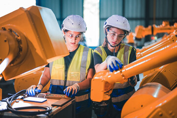Factory engineer woman inspecting on machine with smart tablet. Worker works at machine robot arm....