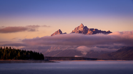 Clouds hanging over Jackson Lake as the sun rises and lights up the tallest peaks of Grand Teton National Park, Wyoming, USA
