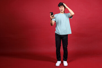Stressed young man with cellphone reading bad news message, touching head in shock and standing on...