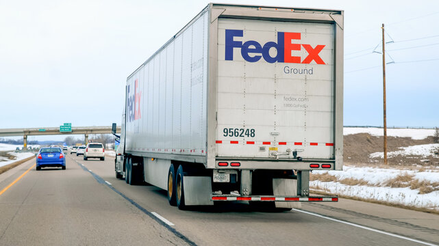 FARIBAULT, MN - 5 MAR 2023: Fed Ex Semi Truck Driving On Freeway, viewed through a car windshield on a Cloudy Day.