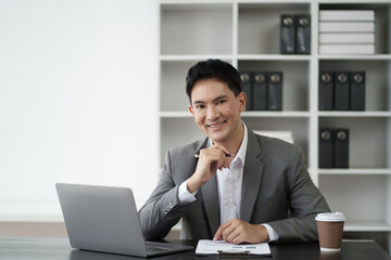 Smart young Asian businessman in grey suit working in the office room with laptop computer.