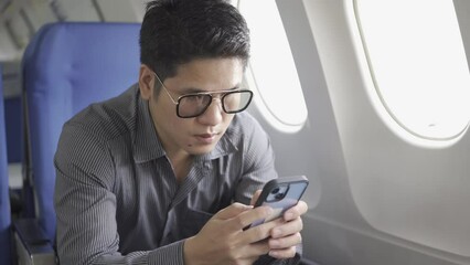 Young Asian businessman passenger using mobile phone to chat with business friend on board during flight. Asian man typing smartphone reading social media and news during business trip.