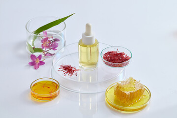 A petri dish of honeycomb with other petri dishes of saffron and fluid are arranged. Glass bottle without label placed on the podium for serum product advertising