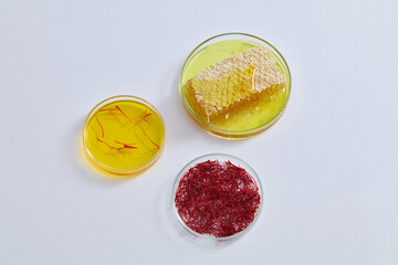 Obraz na płótnie Canvas White background featured three glass petri dishes containing honeycomb, saffron and liquid in yellow color. Saffron is rich in antioxidants