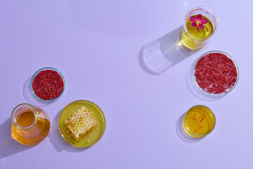 On a purple background, petri dish, beaker and flasks containing stigmas saffron, honey and yellow liquid. Advertising photo with natural ingredient for cosmetic. Empty space for product presentation