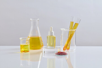 A dropper bottle of serum standing on round podium with several glassware containing yellow fluid surrounded. Empty label for cosmetic product mockup extracted from Saffron