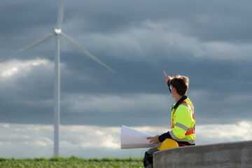Young engineer working on a wind turbine field looking at the blueprint in the middle of the black clouds with sunlight shining, The concept of natural energy from wind.