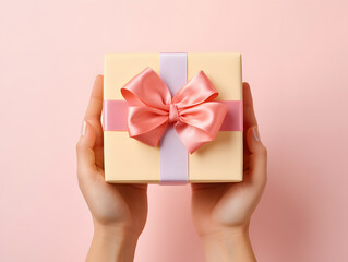 Hands holding gift or present box on pink pastel table top view. Birthday or wedding Concept.