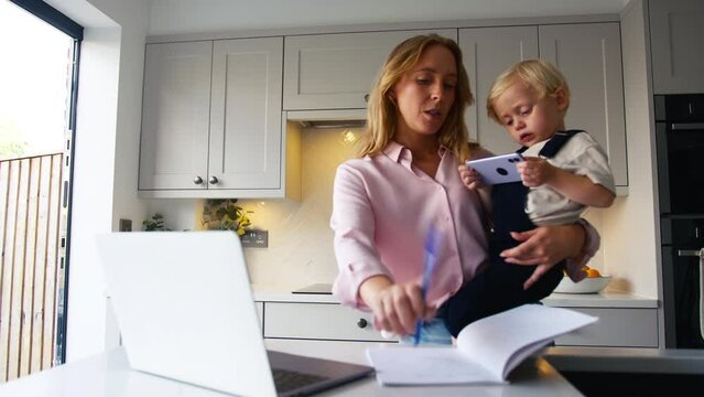Busy working mother looking after young son whilst using laptop and boy plays with her mobile phone - shot in slow motion