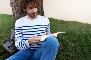 Male university student relaxing on campus.Young man reading book outdoors. Literature and leisure time. Copy space.