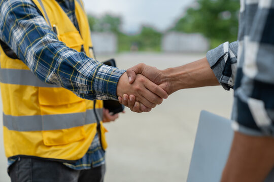 Asian engineer and architect shaking hands at construction site in the outdoor village project Teamwork and a successful housing project.