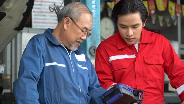 senior asian car mechanic manager training apprentice to checking car engine by Diagnostics Software repair in garage . old asia Auto mechanic teaching trainee or assistant on the repair shop .