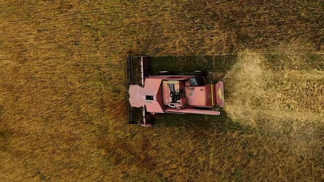 Vertical video war in Ukraine and food crisis, wheat harvest field with shell explosion crater. Drone shot flying over combine harvester working on wheat field