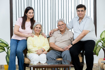 Portrait of Indian family sitting together on sofa in living room and looking towards the camera
