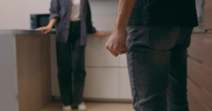Husband with clenched fist goes to wife in fear sitting on floor Back view Woman sits in corner afraid is scared man Blurred background Violence in relationship Man attack threaten wife Cruelty. Slow