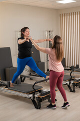 Overweight caucasian woman doing pilates exercises on reformer with personal trainer. 
