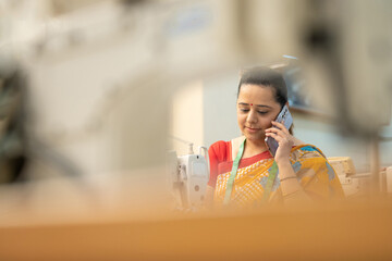 Indian woman talking on smartphone while working at textile factory.
