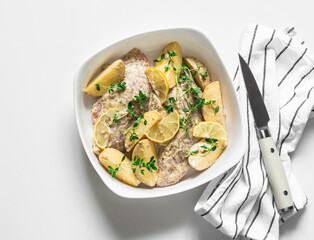 Cooking turkey fillet in mustard-yogurt marinade with new potatoes, lemon and thyme on a light background, top view